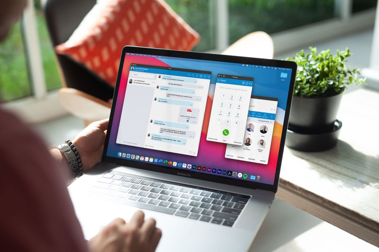 A person is using a laptop with messaging and contact applications on the screen, seamlessly integrating a VoIP phone for business. A small potted plant adds a touch of green to the desk.